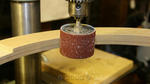 A drum sanding bit installed in the drill press is used to smooth the inside of the rings.